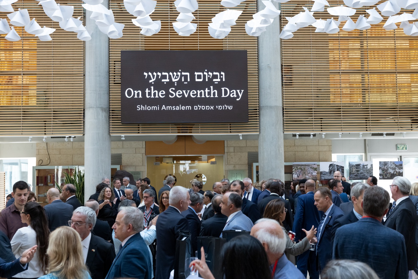 אורחי טקס השקת הספר ״וביום השביעי״ במשרד החוץ בירושלים, מתחת לשלט הספר